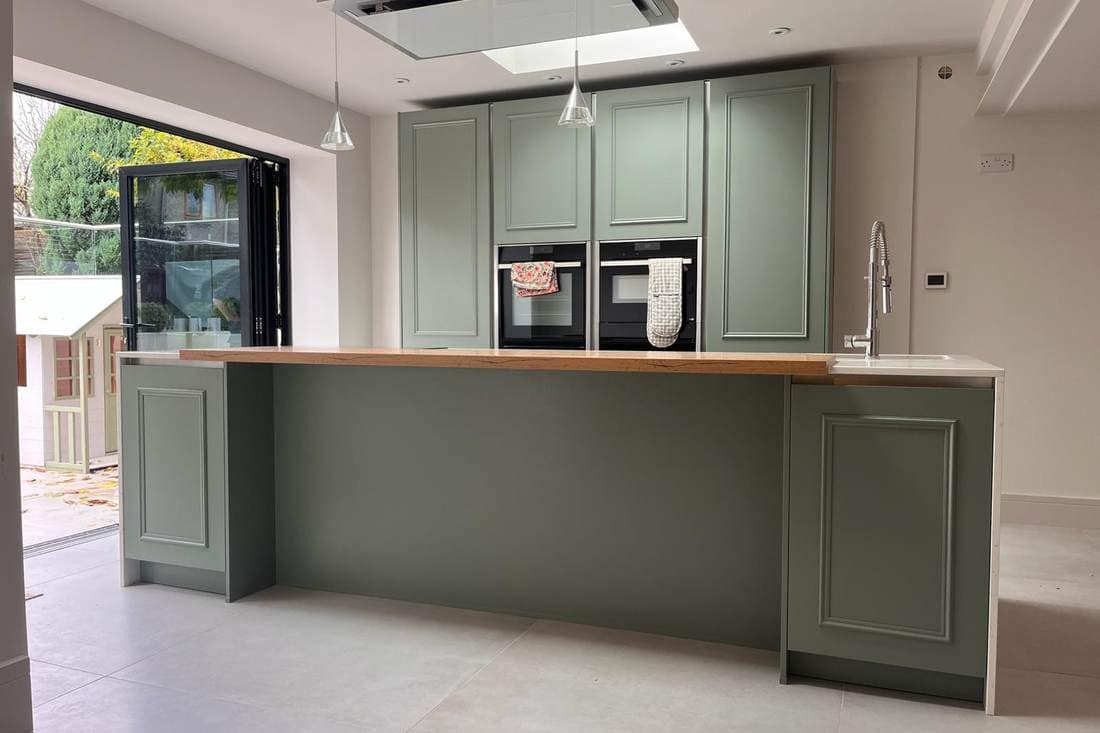 The same island after respraying in sage green, with its oak worktop unchanged