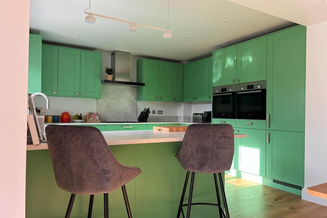 The same kitchen after respraying in a bright green, with bar stools at the island