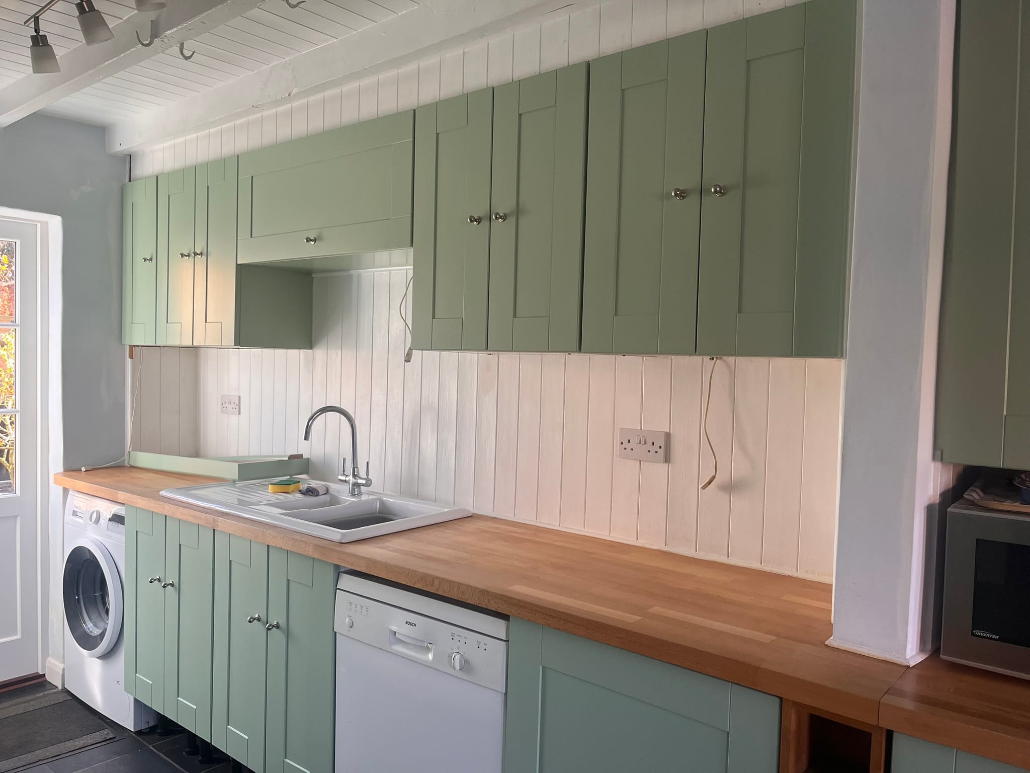 Two-tone sage green kitchen respray with white lower cabinets and a butcher block counter