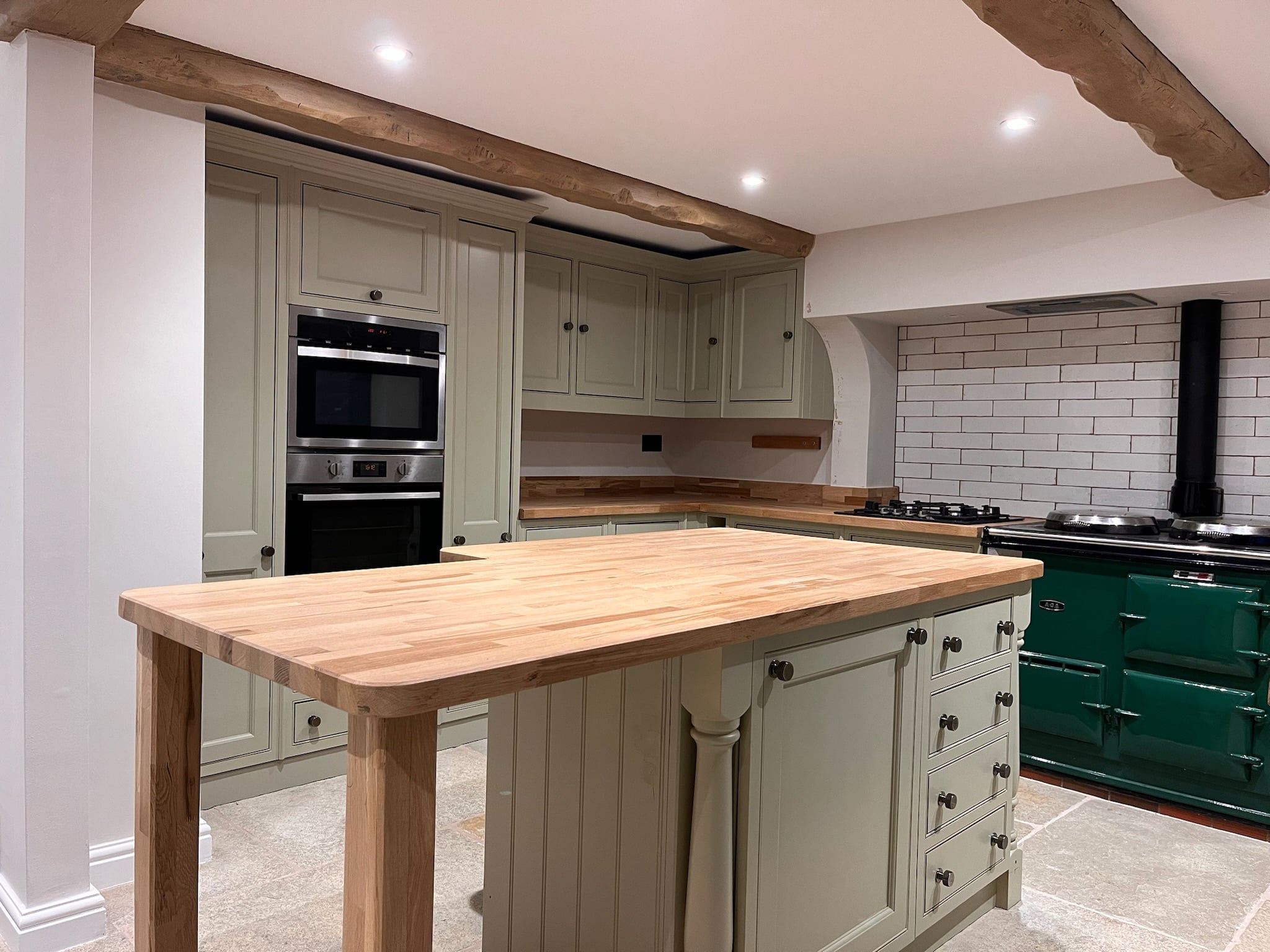 Sage green kitchen after respraying, beneath an exposed timber beam