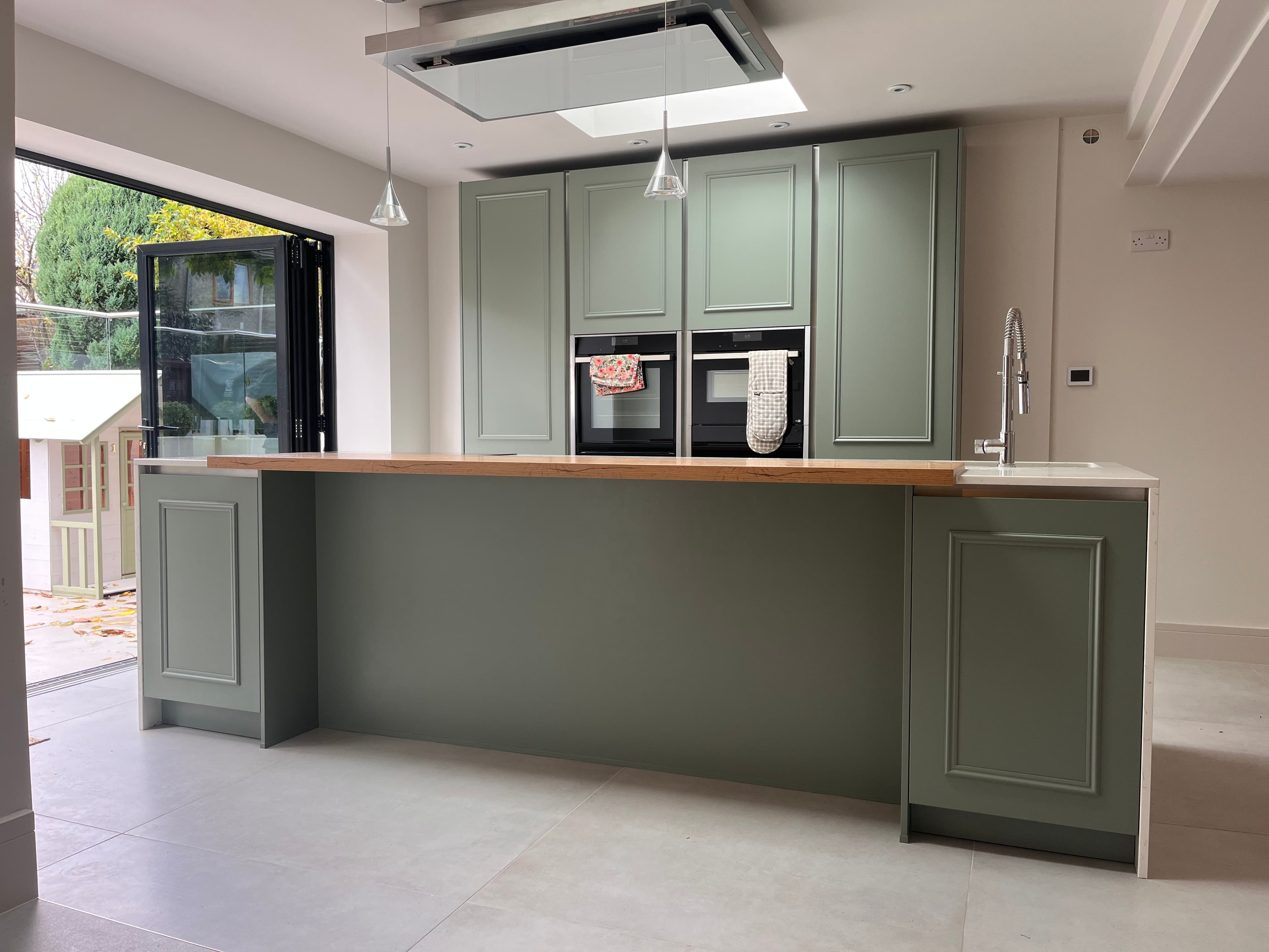 Sage green island kitchen respray with a skylight and integrated double ovens